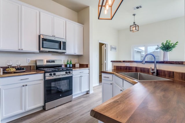 3137 Bent Oak Dr, Mesquite, TX 75181 - kitchen with appliances with stainless steel finishes, a sink, white cabinets, light wood-style flooring, and decorative light fixtures