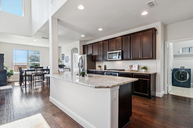 1029 Spring Falls Dr, Mckinney, TX 75071 - kitchen with washer / clothes dryer, stainless steel appliances, arched walkways, light stone countertops, and dark brown cabinets