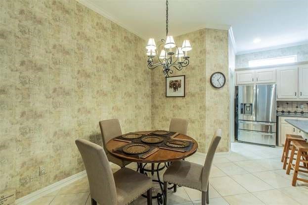 2909 Harkness Dr, Plano, TX 75093 - dining room with wallpapered walls, a chandelier, baseboards, light tile patterned flooring, and ornamental molding