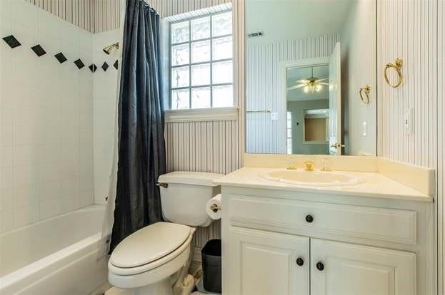 2909 Harkness Dr, Plano, TX 75093 - bathroom featuring wallpapered walls, toilet, vanity, shower / bathtub combination with curtain, and a ceiling fan