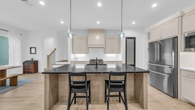 141 Lakeside Dr, Lipan, TX 76462 - kitchen with stainless steel appliances, custom range hood, a kitchen bar, a center island with sink, and light wood-style flooring