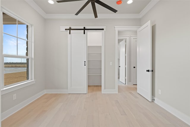 4665 Christie Ave, Caddo Mills, TX 75135 - unfurnished bedroom featuring ornamental molding, light wood finished floors, a barn door, baseboards, and a walk in closet