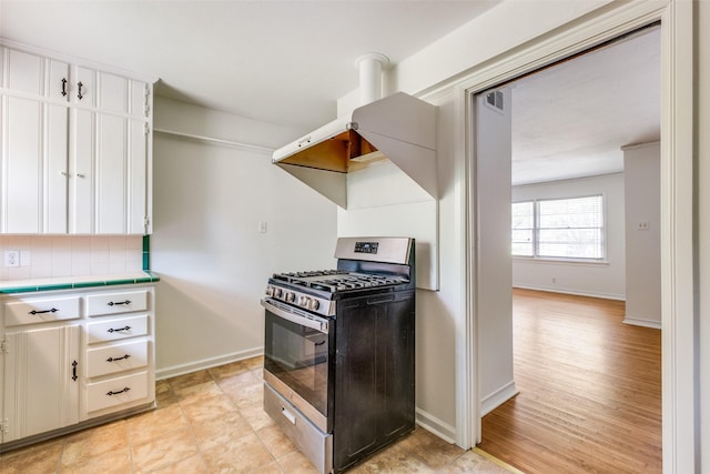 2109 Blake Ave, Dallas, TX 75228 - kitchen featuring stainless steel gas range oven, tile counters, decorative backsplash, baseboards, and white cabinets