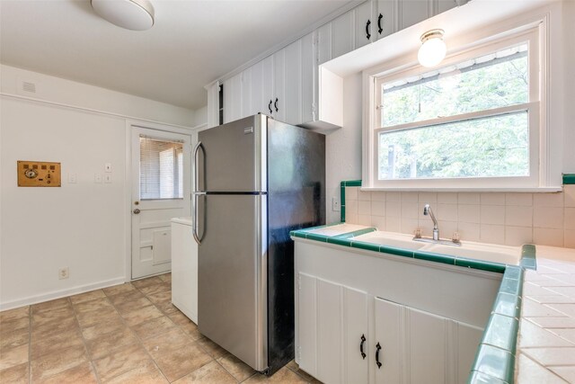2109 Blake Ave, Dallas, TX 75228 - kitchen with tile countertops, freestanding refrigerator, decorative backsplash, a sink, and white cabinetry