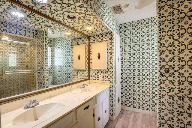 201 Brookhaven Ter, Commerce, TX 75428 - bathroom with wallpapered walls, double vanity, a textured ceiling, toilet, and wood finished floors