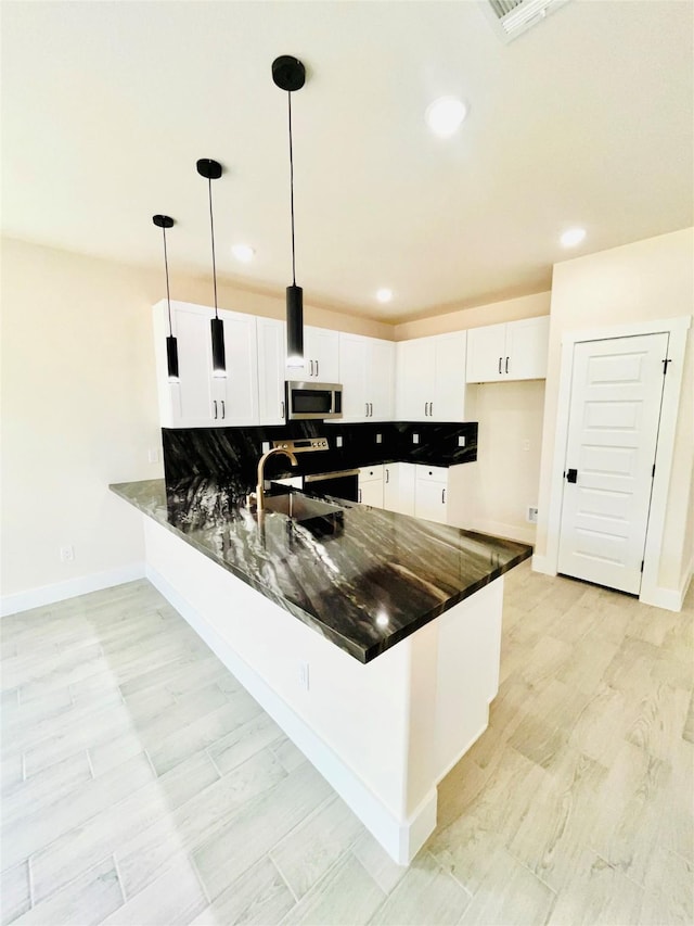 2309 Forest Hill Ln, Granbury, TX 76048 - kitchen featuring stainless steel microwave, a peninsula, dark stone counters, recessed lighting, and baseboards