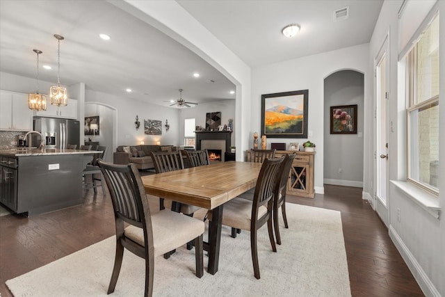 309 Bluffside Trl, Benbrook, TX 76126 - dining room with arched walkways, a warm lit fireplace, ceiling fan, dark wood-style flooring, and healthy amount of natural light