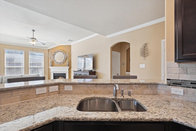 200 Baldwin Dr, Fate, TX 75189 - kitchen featuring a sink, open floor plan, ornamental molding, a ceiling fan, and a lit fireplace