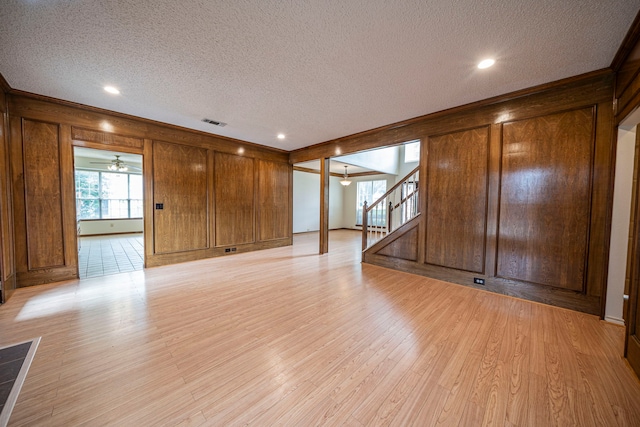 4404 Bentley Dr, Plano, TX 75093 - unfurnished living room with a textured ceiling, wood walls, stairway, light wood-type flooring, and ceiling fan