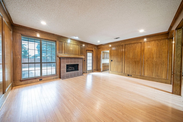 4404 Bentley Dr, Plano, TX 75093 - unfurnished living room featuring a textured ceiling, wooden walls, light wood finished floors, a tiled fireplace, and ornamental molding