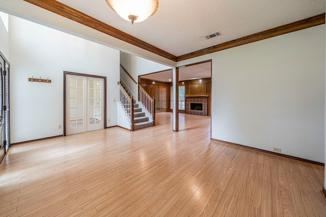 4404 Bentley Dr, Plano, TX 75093 - spare room featuring stairway, a textured ceiling, a brick fireplace, light wood-style flooring, and crown molding