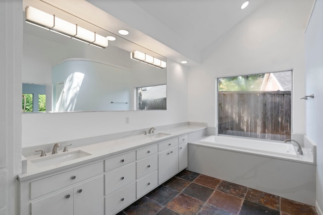 8907 Club Creek Cir, Dallas, TX 75238 - bathroom with stone tile floors, double vanity, a garden tub, lofted ceiling, and recessed lighting
