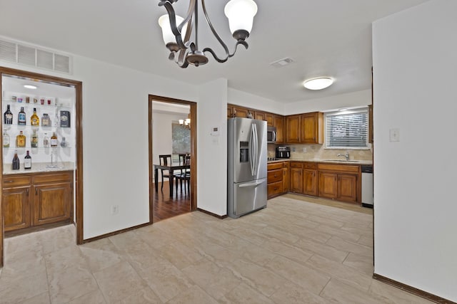 1614 Shadow Moss Way, Carrollton, TX 75007 - kitchen featuring appliances with stainless steel finishes, a chandelier, brown cabinetry, and tasteful backsplash