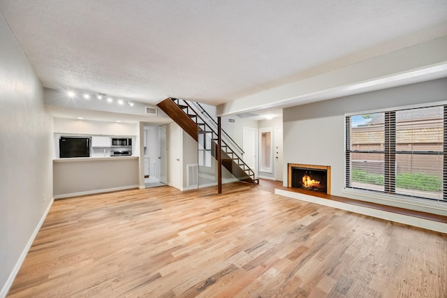 3121 Park Ln Unit 1103, Dallas, TX 75220 - unfurnished living room with light wood-type flooring, a warm lit fireplace, stairs, baseboards, and a textured ceiling