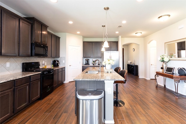 2400 Prairie Trail Ave, Aubrey, TX 76227 - kitchen with black appliances, a sink, arched walkways, dark brown cabinets, and dark wood finished floors