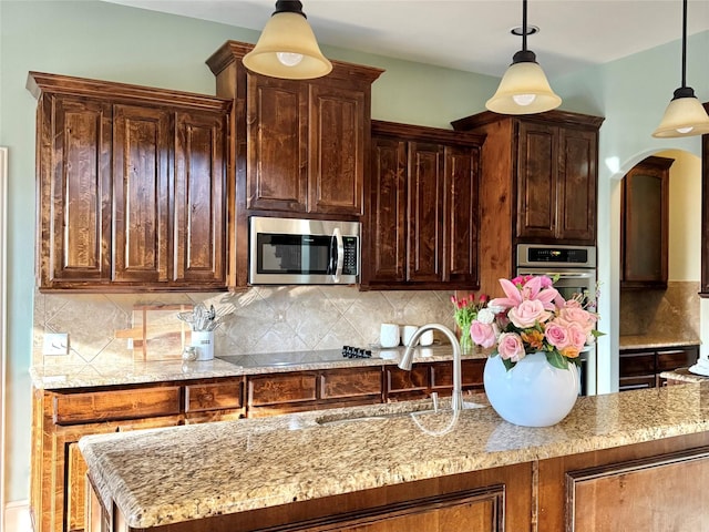 1801 Monaco Dr, Corinth, TX 76210 - kitchen with appliances with stainless steel finishes, a sink, arched walkways, decorative light fixtures, and decorative backsplash