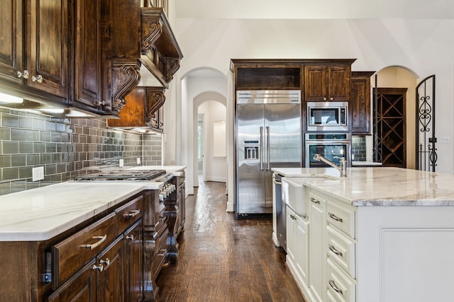 3708 Ledgestone Ct, Richardson, TX 75082 - kitchen featuring built in appliances, arched walkways, white cabinets, light stone countertops, and decorative backsplash