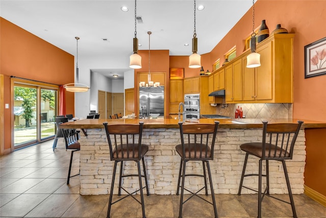 1212 Porter Rd, Bartonville, TX 75022 - kitchen featuring appliances with stainless steel finishes, a peninsula, under cabinet range hood, backsplash, and pendant lighting