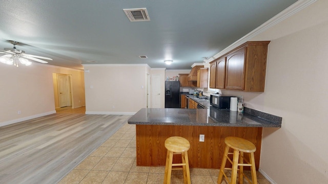 2008 Pine Knot Dr, Heartland, TX 75126 - kitchen with black appliances, a peninsula, brown cabinets, a kitchen bar, and dark stone countertops