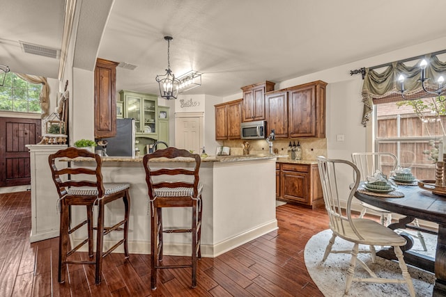 1702 Clarke Springs Dr, Allen, TX 75002 - kitchen with appliances with stainless steel finishes, a chandelier, a breakfast bar, dark wood finished floors, and brown cabinetry
