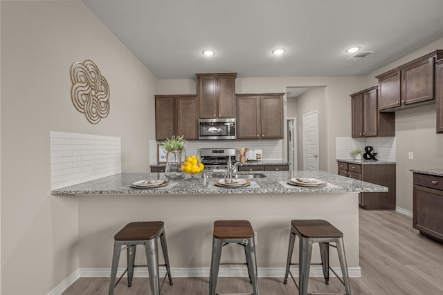 1601 Bennington Ln, Celina, TX 75009 - kitchen with appliances with stainless steel finishes, tasteful backsplash, a breakfast bar, light wood finished floors, and a peninsula