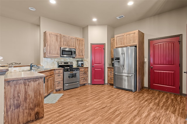 4905 Lakepark Dr, Sanger, TX 76266 - kitchen with appliances with stainless steel finishes, a sink, a peninsula, light wood finished floors, and backsplash