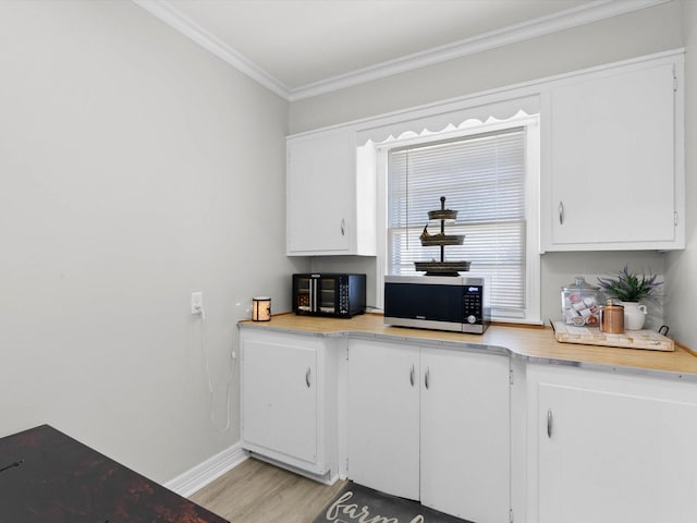 910 N Mill St, Bowie, TX 76230 - kitchen with stainless steel microwave, light countertops, ornamental molding, white cabinetry, and light wood-style flooring