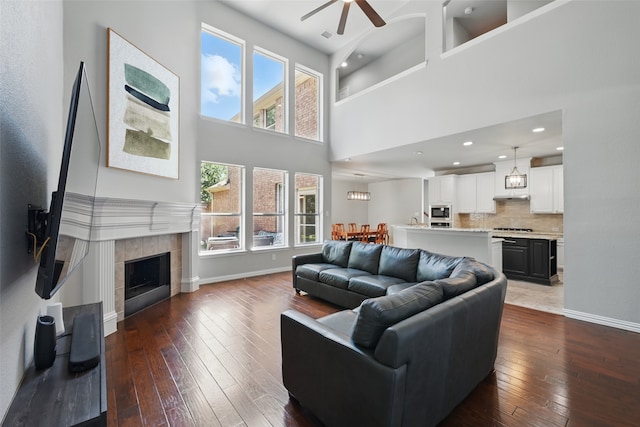 14877 Snowshill Dr, Frisco, TX 75035 - living area with dark wood-style flooring, ceiling fan, a towering ceiling, baseboards, and a fireplace