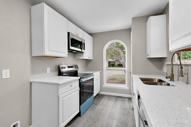6821 Mickey Dr, Watauga, TX 76148 - kitchen with appliances with stainless steel finishes, light wood finished floors, a sink, white cabinetry, and light countertops