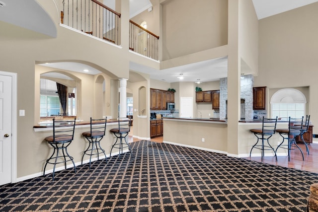 8 Calloway Ct, Mansfield, TX 76063 - kitchen with carpet, a kitchen bar, a towering ceiling, brown cabinetry, and arched walkways