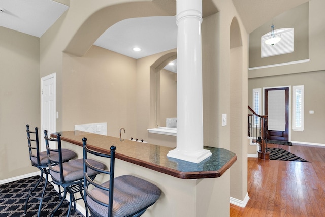 8 Calloway Ct, Mansfield, TX 76063 - kitchen featuring arched walkways, baseboards, wood finished floors, a breakfast bar area, and decorative columns