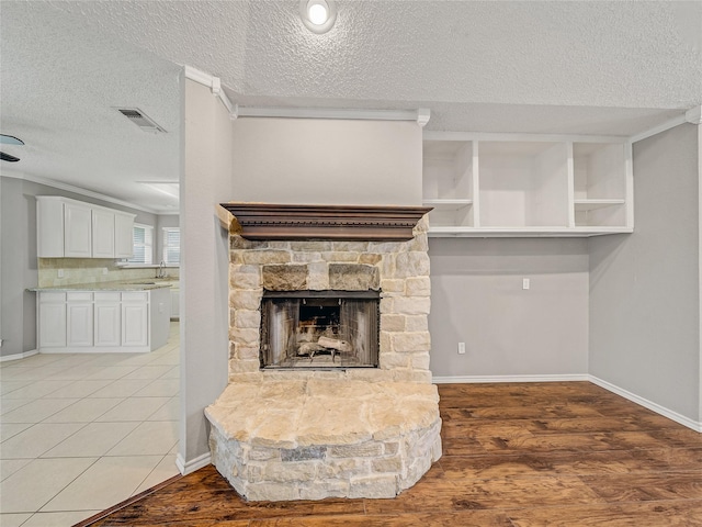 7900 Marsh Ct, Fort Worth, TX 76123 - unfurnished living room featuring a textured ceiling, a fireplace, baseboards, a sink, and light wood finished floors