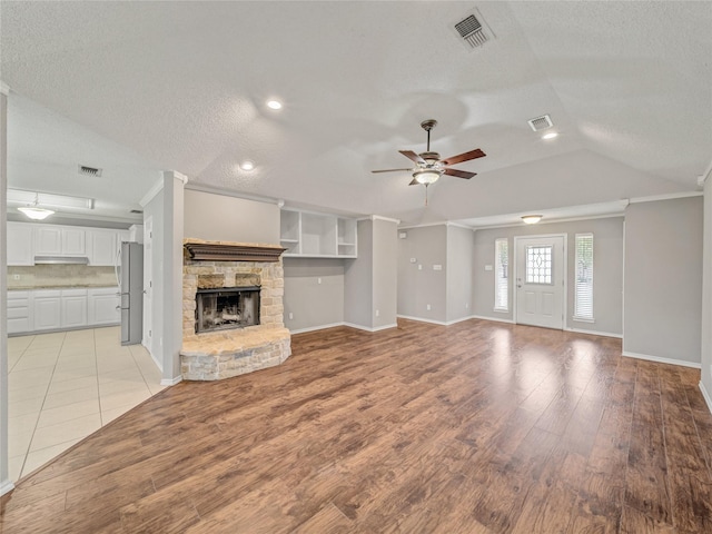 7900 Marsh Ct, Fort Worth, TX 76123 - unfurnished living room with ceiling fan, light wood-style flooring, a stone fireplace, a textured ceiling, and baseboards