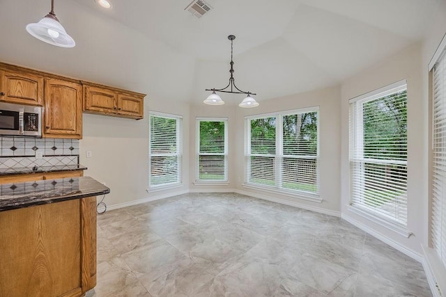 230 Mitchell Blvd, Weatherford, TX 76087 - kitchen with stainless steel microwave, brown cabinetry, pendant lighting, tasteful backsplash, and high vaulted ceiling