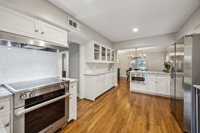 6443 Velasco Ave, Dallas, TX 75214 - kitchen with stainless steel appliances, white cabinetry, tasteful backsplash, glass insert cabinets, and a chandelier