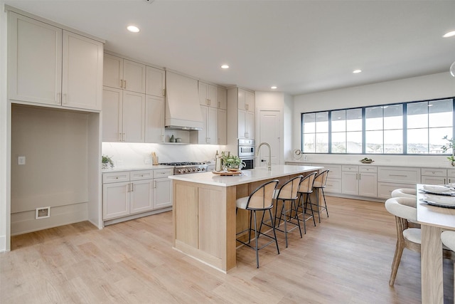 4513 Fair Creek Ter, Fort Worth, TX 76008 - kitchen with custom exhaust hood, light wood finished floors, a breakfast bar area, light countertops, and backsplash