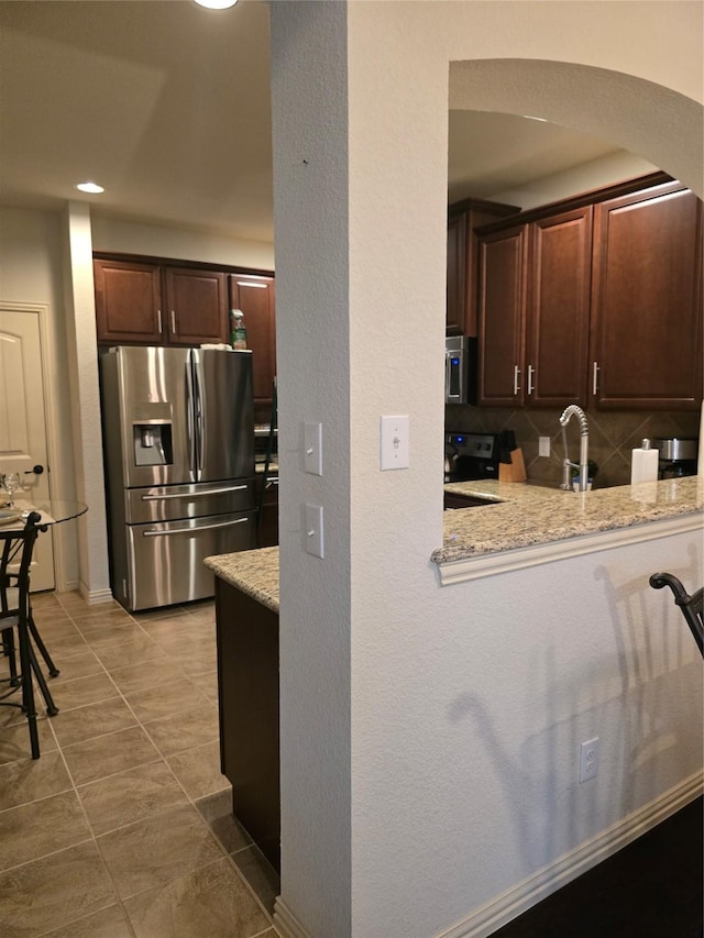 6936 Pascal Way, Fort Worth, TX 76137 - kitchen featuring stainless steel appliances, arched walkways, dark brown cabinets, light stone countertops, and tile patterned flooring