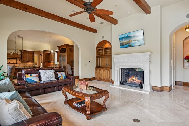 6203 Sweeney Trl, Frisco, TX 75034 - living area with arched walkways, beamed ceiling, ceiling fan, baseboards, and a warm lit fireplace