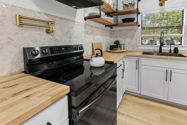 207 W River, Meridian, TX 76665 - kitchen featuring black range with electric stovetop, butcher block countertops, a sink, decorative backsplash, and light wood-style floors