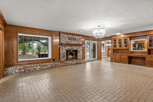1108 Quitman St, Pittsburg, TX 75686 - unfurnished living room featuring a chandelier, wooden walls, healthy amount of natural light, a brick fireplace, and crown molding
