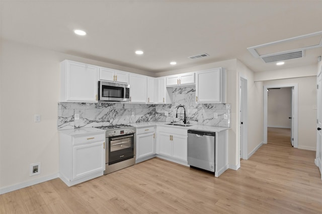 2634 Macon St, Dallas, TX 75215 - kitchen featuring appliances with stainless steel finishes, white cabinetry, tasteful backsplash, light wood-style flooring, and recessed lighting