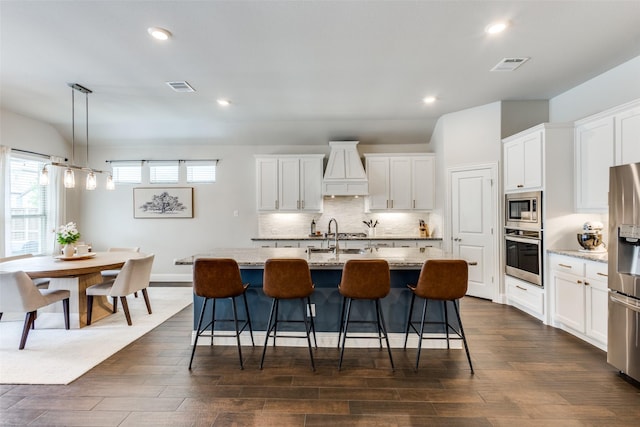 2921 Crossbow Ln, Celina, TX 75009 - kitchen with stainless steel appliances, premium range hood, white cabinets, decorative backsplash, and dark wood-style floors