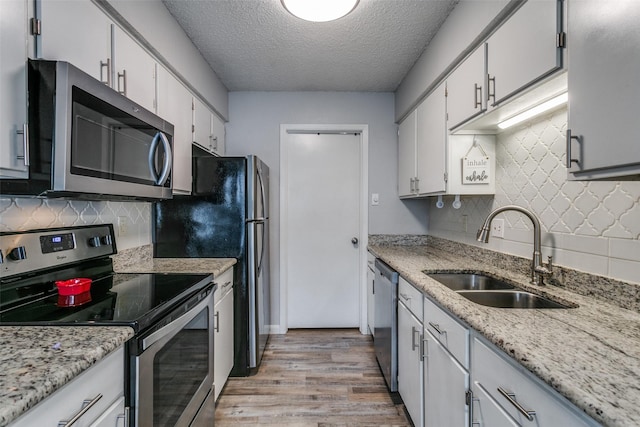 649 Timberline Dr, Hurst, TX 76053 - kitchen with stainless steel appliances, a sink, light wood-type flooring, a textured ceiling, and backsplash