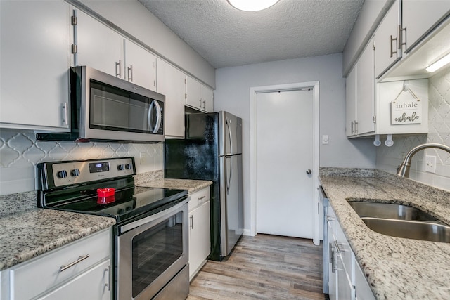 649 Timberline Dr, Hurst, TX 76053 - kitchen with stainless steel appliances, a sink, a textured ceiling, light wood-style floors, and tasteful backsplash