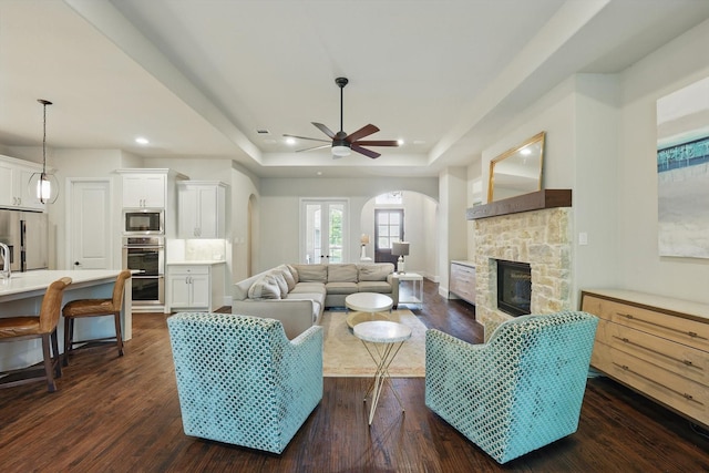 125 Chisholm Trl, Highland Village, TX 75077 - living room featuring arched walkways, a fireplace, a ceiling fan, dark wood-style floors, and a raised ceiling