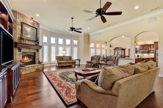 128 Whispering Winds Dr, Gunter, TX 75058 - living area with crown molding, a stone fireplace, a ceiling fan, arched walkways, and dark wood finished floors