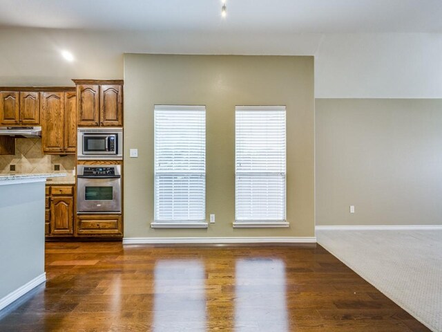 3604 Camino Trl, Mckinney, TX 75070 - kitchen with stainless steel appliances, brown cabinets, dark wood finished floors, backsplash, and under cabinet range hood