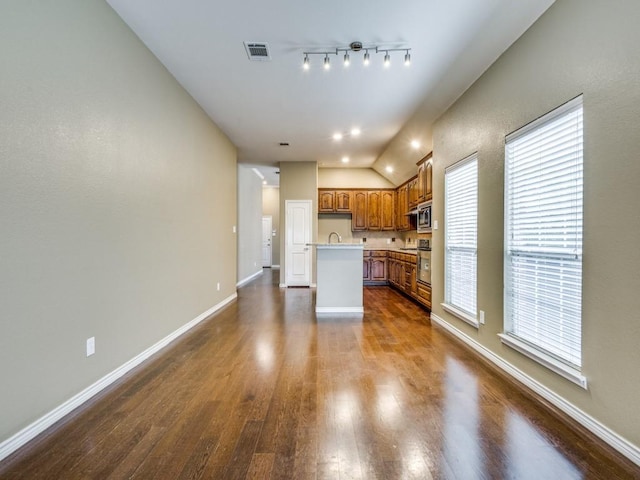3604 Camino Trl, Mckinney, TX 75070 - kitchen with brown cabinets, dark wood-type flooring, baseboards, appliances with stainless steel finishes, and lofted ceiling