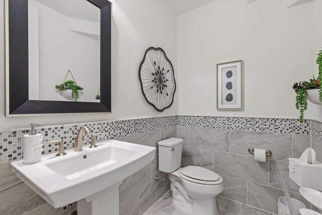 10933 Smoky Oak Trl, Flower Mound, TX 76226 - half bathroom featuring tile walls, toilet, wainscoting, a sink, and marble finish floors