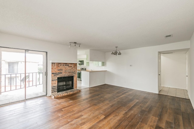 920 Turtle Cv Unit 252, Irving, TX 75060 - unfurnished living room with wood finished floors, a brick fireplace, a textured ceiling, a chandelier, and rail lighting